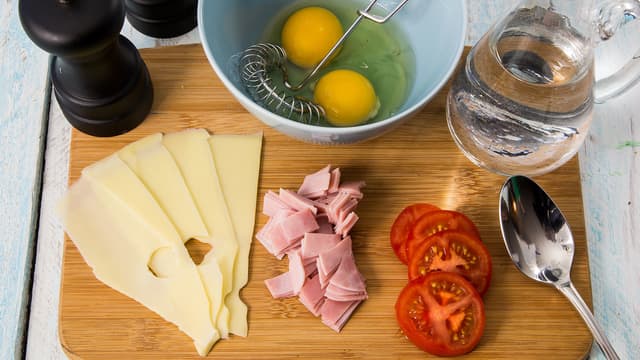 Skjær tomaten i skiver og skinkeskivene i små biter. Skjær 3-4 skiver av gulosten.