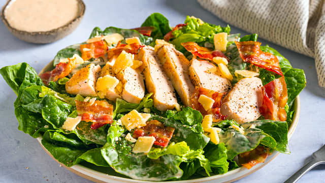 Topp salaten med kylling, bacon, sprø krutonger og dressing.