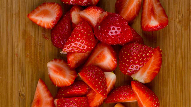 Skyll jordbærene og skjær vekk det grønne. Del jordbærene og fordel i skåler.