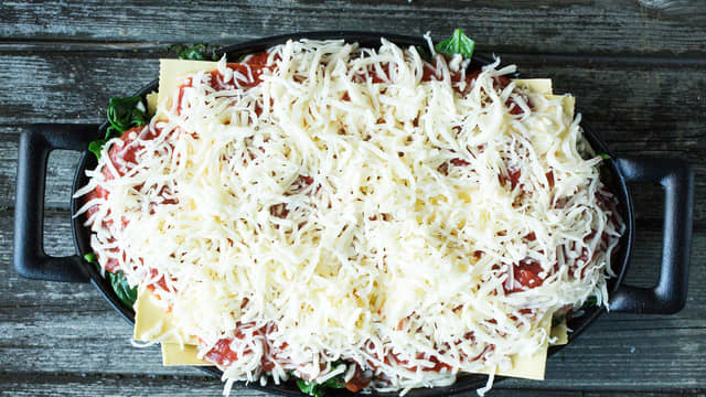 Legg på den siste pastaplaten og fordel resten av cottage cheese-blandingen og tomatsausen på toppen. Dryss over revet ost.