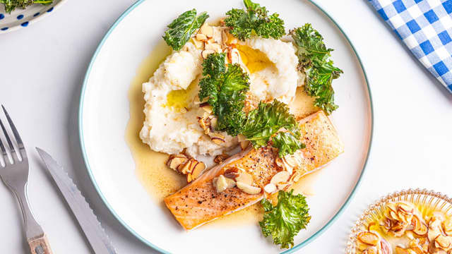 Anrett blomkålpuré, laks og grønnkålchips på tallerkener og topp med mandelflak og smør.