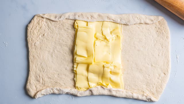 Skjær smøret i skiver, eller bruk en ostehøvel. Legg halvparten av smøret på midten av firkanten. Brett de to delene uten smør på over smøret. Pass på å brette inn litt deig på endene, slik at smøret er pakket inn i deig.