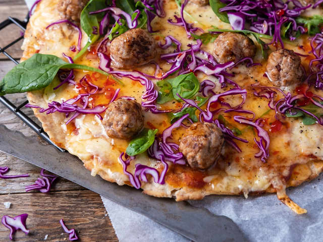Topp pizzaen med babyspinat og rødkål kuttet i tynne strimler før servering.