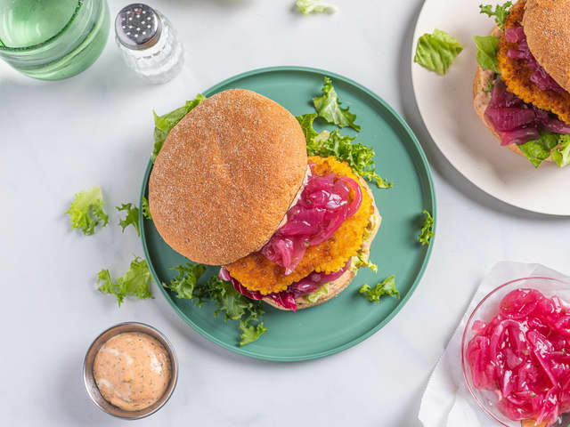 Anrett bunnene på burgerbrødene på to tallerkener og topp med syltet rødløk, salat og fiskeburger. Legg på toppen av burgerbrødet.