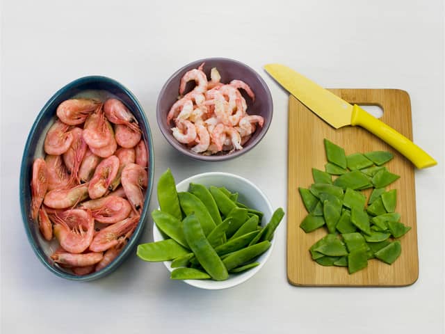 Kok pasta etter anvisning på pakken. Pill reker og skjær sukkererter i biter.