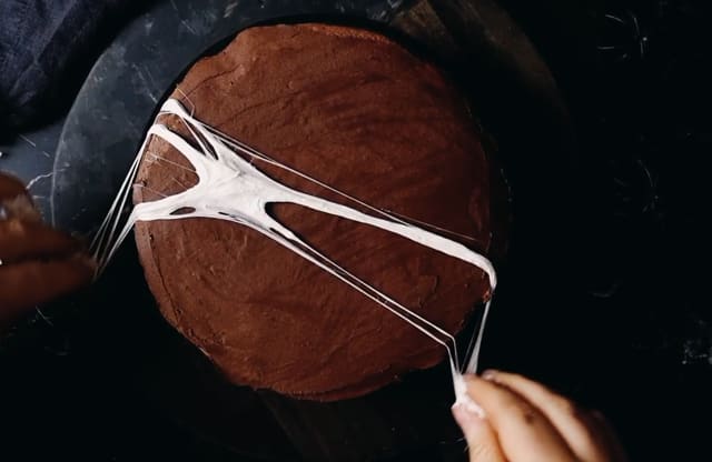 Når marshmellowstrådene er lange nok, legger du dem ned på kaken. Gjenta til du har fått kul spindelvevpynt på hele kaken.