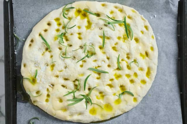 Ha deigen på et stekebrett med bakepapir og trykk den utover med fingrene. Hell over god olivenolje og press masse hull i deigen med fingrene. Dryss over havsalt og rosmarin.