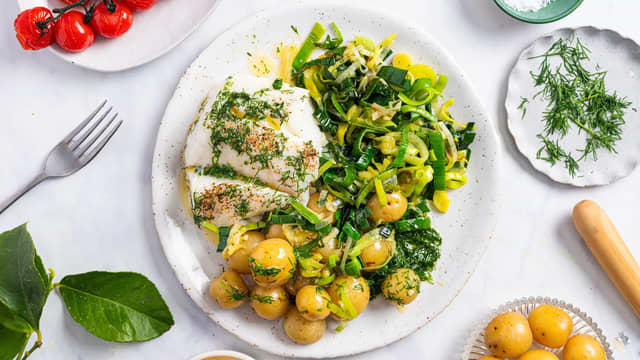 Server skreiloinen med stekt purre, kokte poteter, bakte tomater og urtesmør.