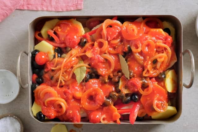 Hell halvparten av blandingen over i en ildfast form. Legg over halvparten av potetene, så klippfisk, paprika, og resten av potetene. Krydre med salt og pepper, og fordel sorte oliven over. Så heller du resten av tomatblandingen over det hele og har i 2 laurbærblad for ekstra god smak.