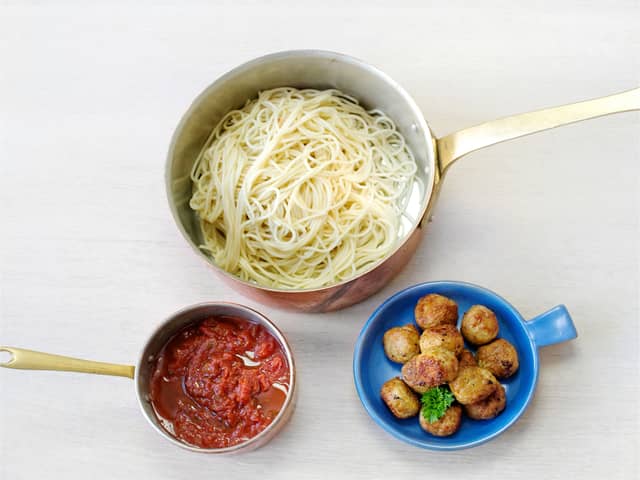 Kok spagetti etter anvisning på pakken, varm pastasausen i en kjele og anrett på tallerkener med noen kjøttboller på toppen.