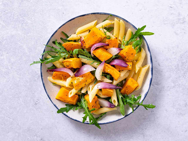 Anrett salaten med pasta, gresskar, rødløk og ruccula og topp med en skvis av den bakte sitronen.