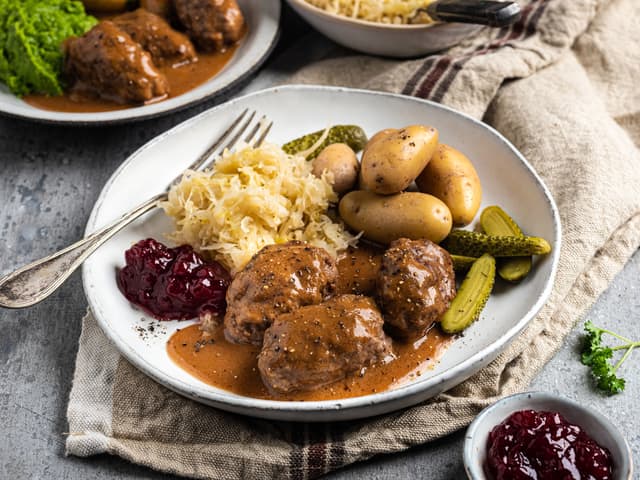 Server de hjemmelagde kjøttkakene med ertestuing, brun saus, nykokte poteter og tyttebærsyltetøy.