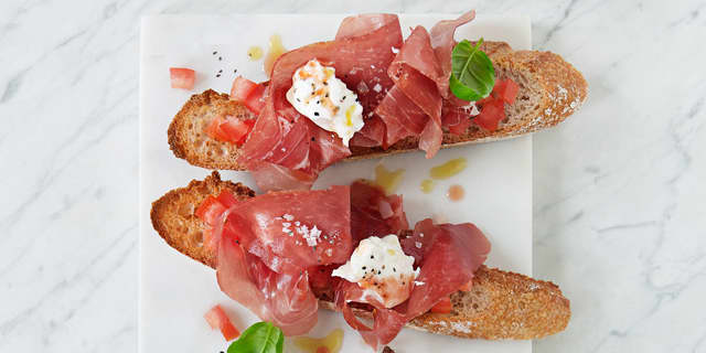Fordel tomatene utover brødet. Legg på 2 skiver skinke på hver brødskive og en «dæsj» mozzarella. Ha over litt basilikum, olivenolje, salt og pepper på toppen!