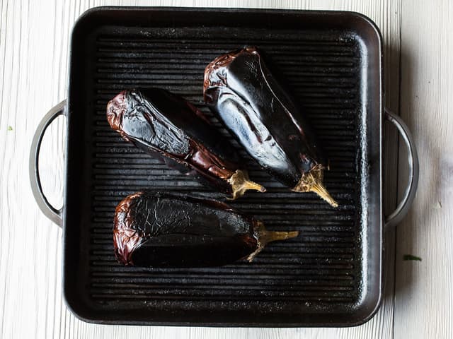 Legg hele auberginer på grillen eller i en varm jernpanne. Grill auberginene over middels høy varme til de blir helt myke over det hele, det tar ca. 1 time. Snu auberginene etter hvert som du ser de faller sammen. Er du usikker på om de er ferdige, kan du la dem ligge litt til.