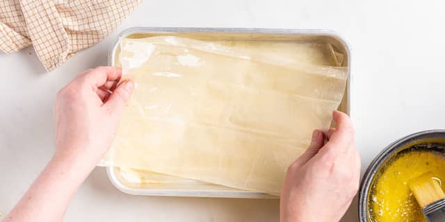 Pensle et ark filodeig med smør, og legg det i bunnen av formen. Pensle neste ark og legg det oppå det første. Fortsett til du har 10 lag filodeig med smør imellom.