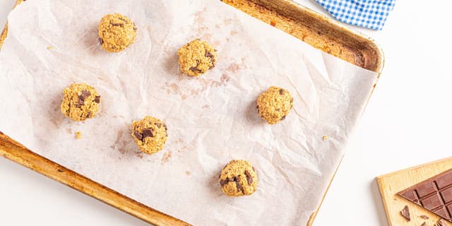 Rull sammen boller av deigen med hendene og legg bollene på et bakebrett med bakepapir. Klem bollene flate.