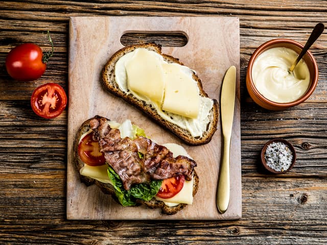 Smør aioli på begge skivene. Legg tre skiver ost på den ene skiven og topp med tomatskiver, salat og sprøstekt bacon. Krydre med salt og pepper.