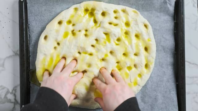 Når deigen har hevet ferdig, lager du groper i deigen med fingrene. Hell så over urteoljen, og dryss over flaksalt.
Del tomatene i to og stikk dem godt ned i focaccia deigen.