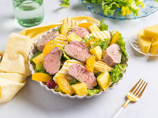 Anrett romanosalaten på to tallerkener eller et fat. Topp med ananas, halloumi, appelsin, svinefilet og olivenolje.