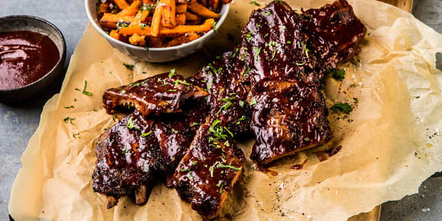 Server grillet spareribs med fylte tomater, søtpotetfries og coleslaw.