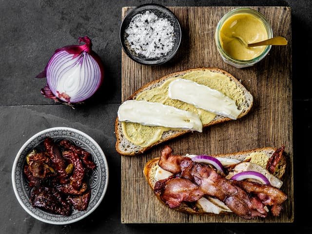 Legg skivet rødløk, soltørket tomat, kylling og sprøstekt bacon på, og topp med to osteskiver og en skive brød som har sennepsiden ned. Krydre med salt og pepper.