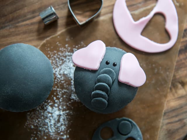 Hull ut flere små sirkler til snablen og hull ut hjerter av rosa fondant til elefantører. Øyne tegnes på med farget glasur.