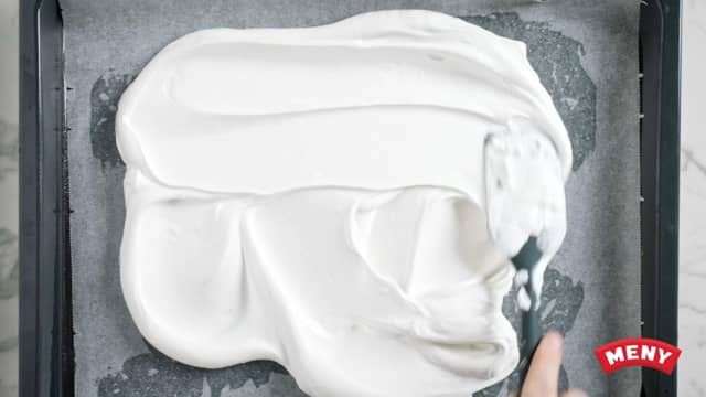 Når marengsen er blank og smidig smører du den forsiktig utover et bakepapir på et stekebrett med en slikkepott.