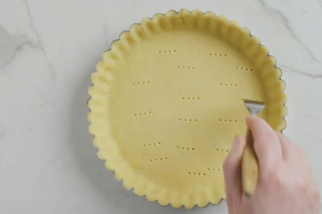 Kjevle så ut deigen og kle en form, ca 24 cm, helt opp til kantene, bruk ildfast paiform eller kakeform. Fjern eventuelt overflødig deig. Prikk bunnen med en gaffel. Stek bunnen midt i ovnen ved 200 grader i 15 minutter.