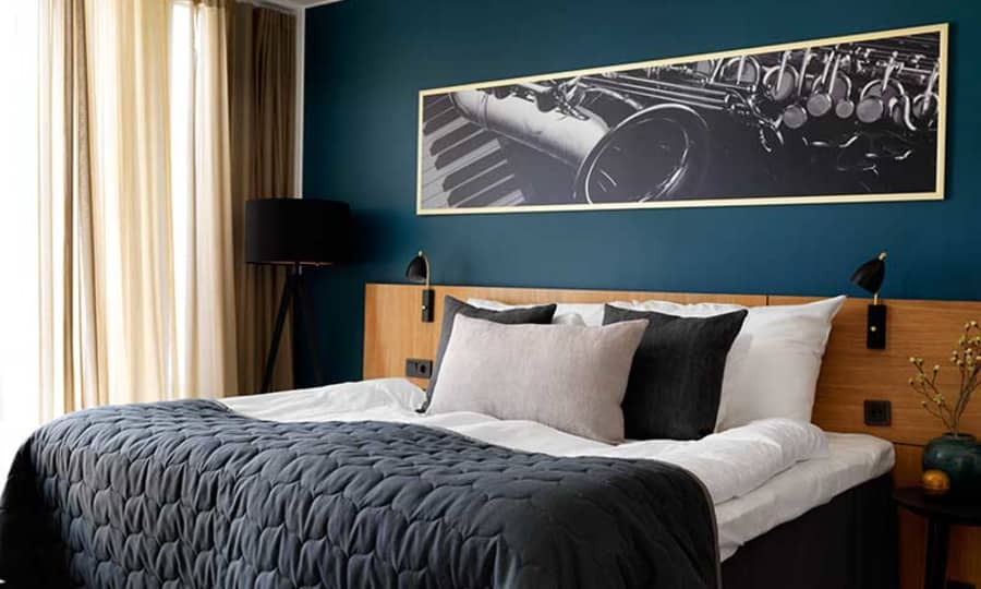 Hotellrom med stor seng og mørkegrønn vegg med bilde