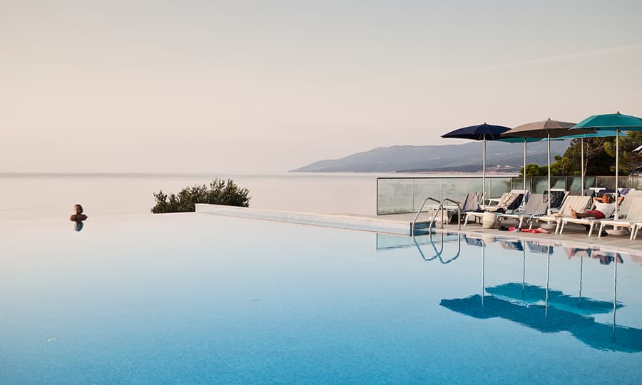 Dame som sitter å speider ut over havet i et infinity pool