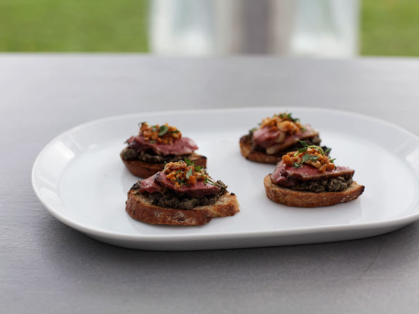 Revens håndholdte duebryster på en seng av oliventapenade Revens håndholdte duebryster på en seng av oliventapenade
