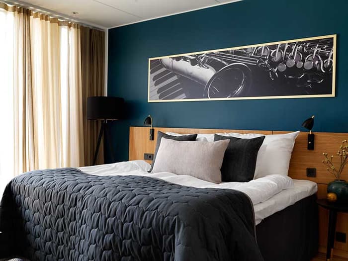 Hotellrom med stor seng og mørkegrønn vegg med bilde