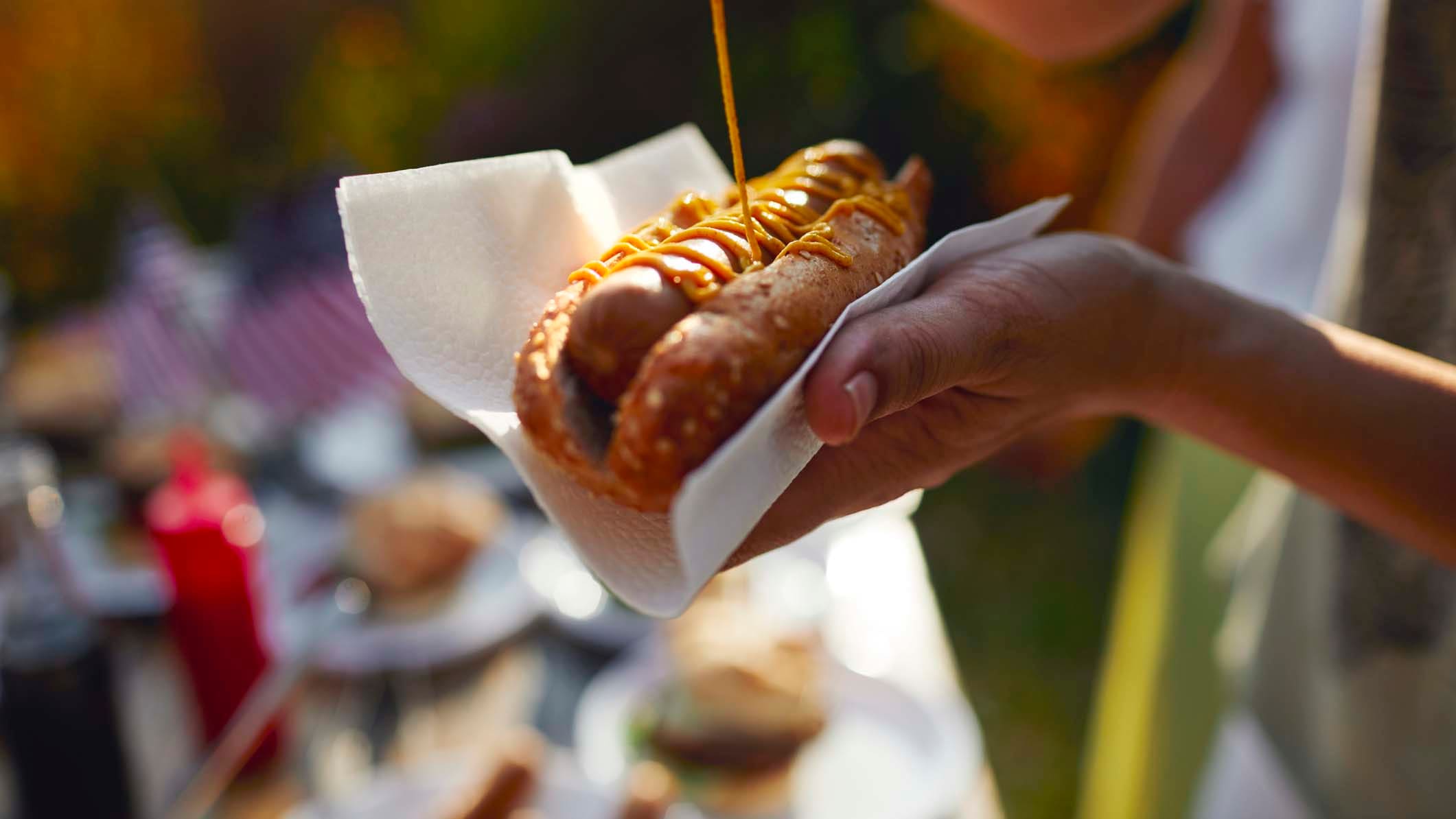 Noen tar på sennep på grillpølse i brød