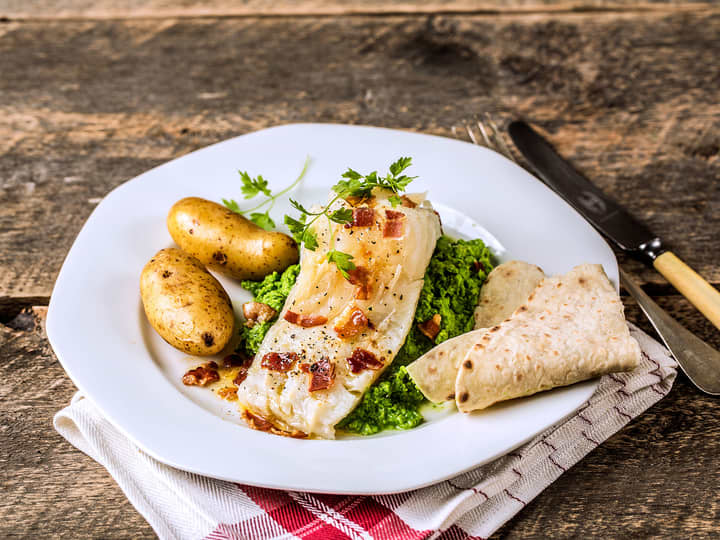 Server lutefisk med tradisjonelt tilbehør som  sprøstekt bacon og nykokte poteter.