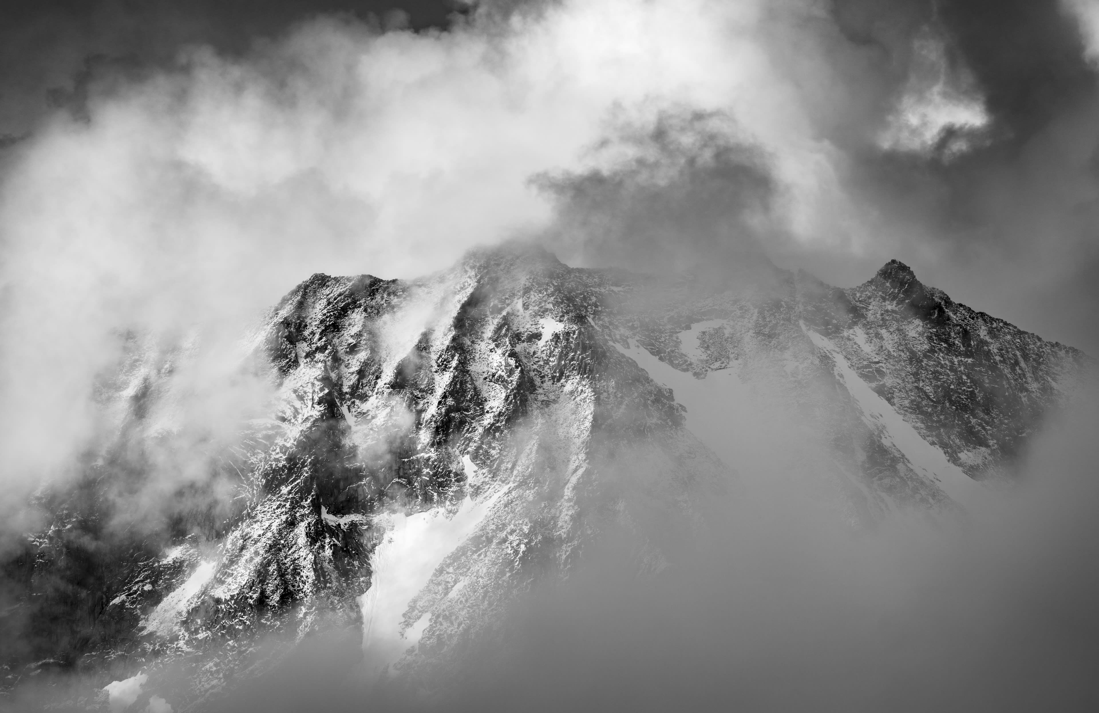 A black and white photo of a mountain peak partially obscured by clouds and fog.