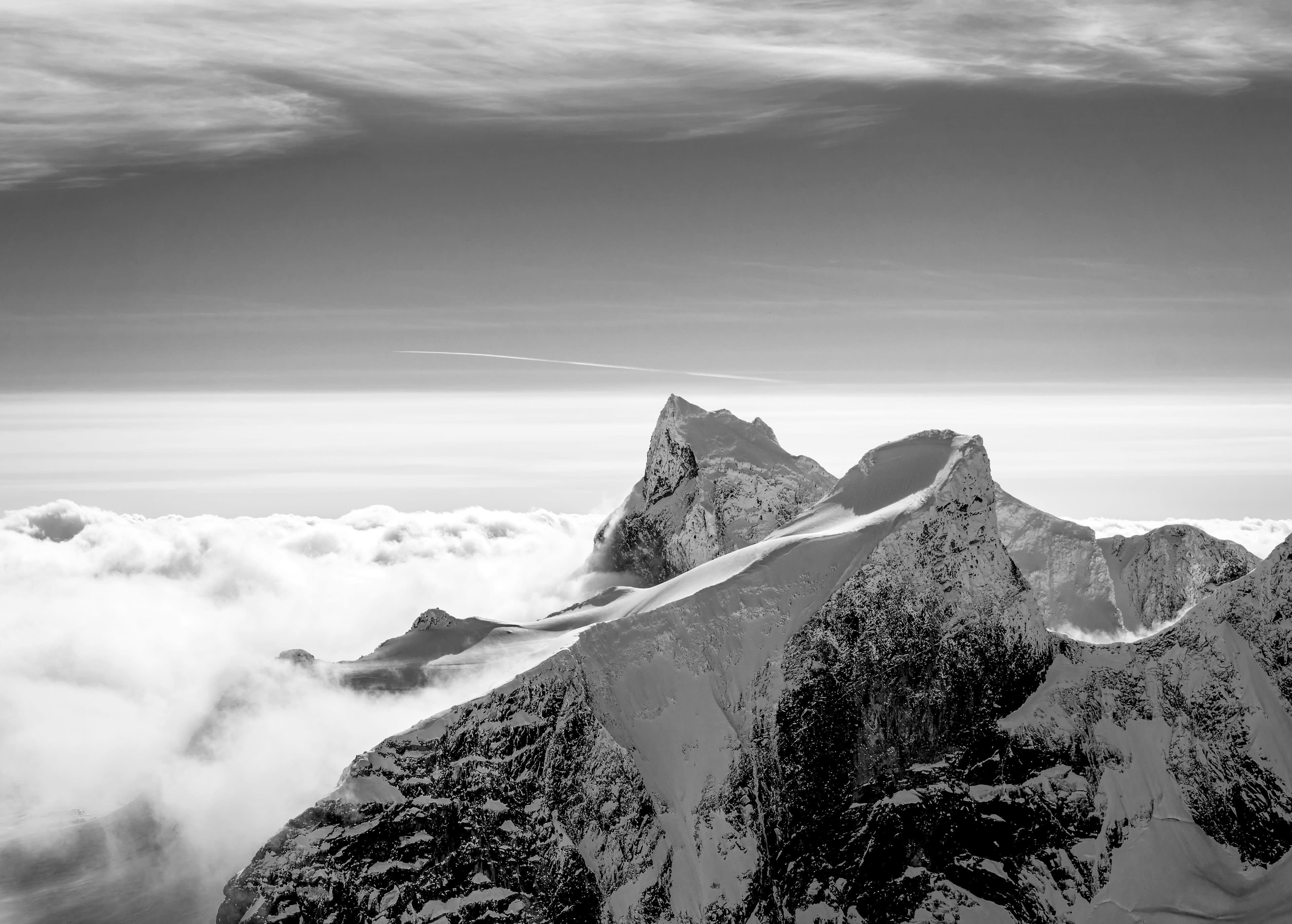A black and white photo of a snow-covered mountain peak rising above a sea of clouds.  

