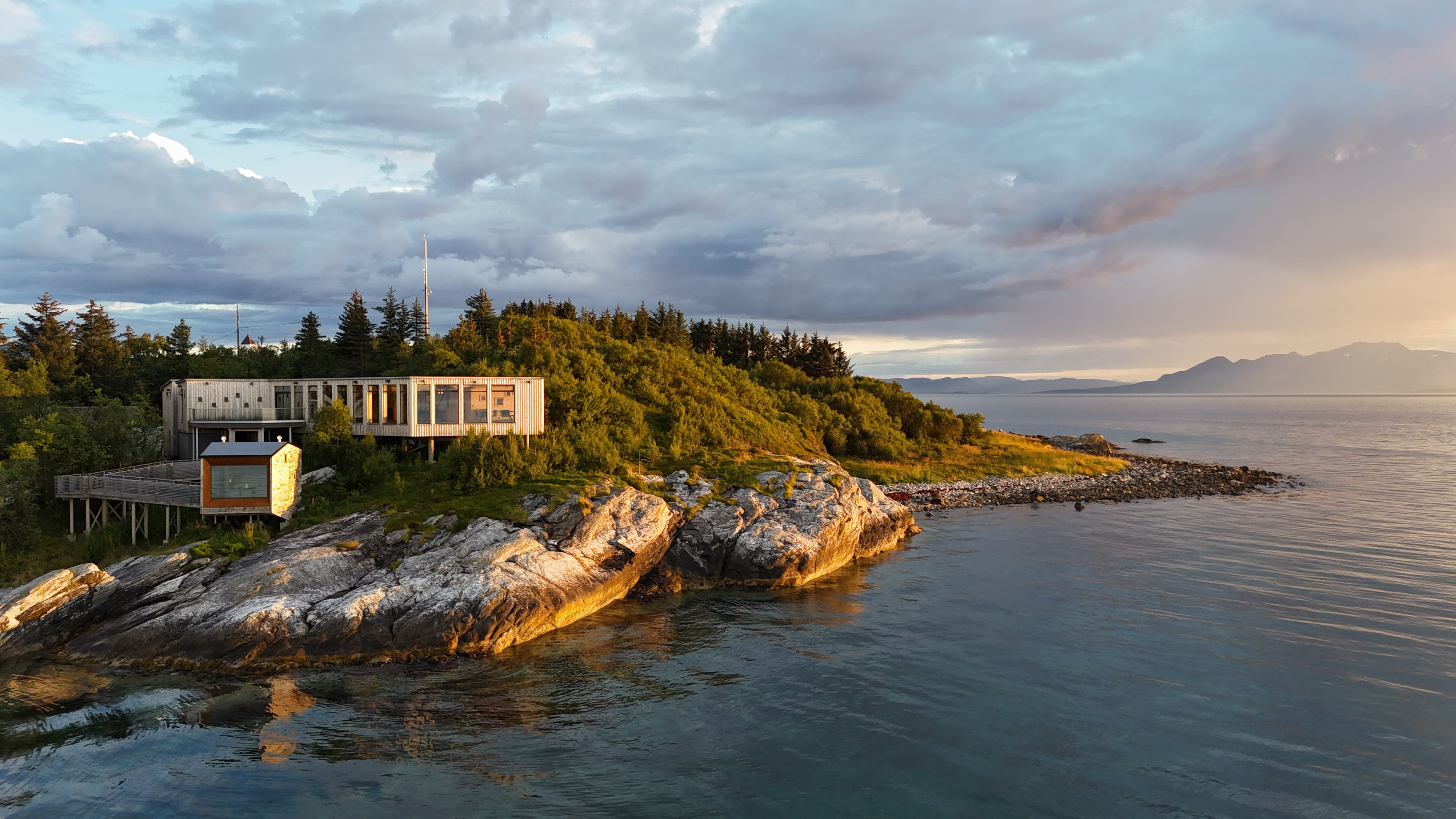 Modern wooden building on a rocky coastline at sunset.