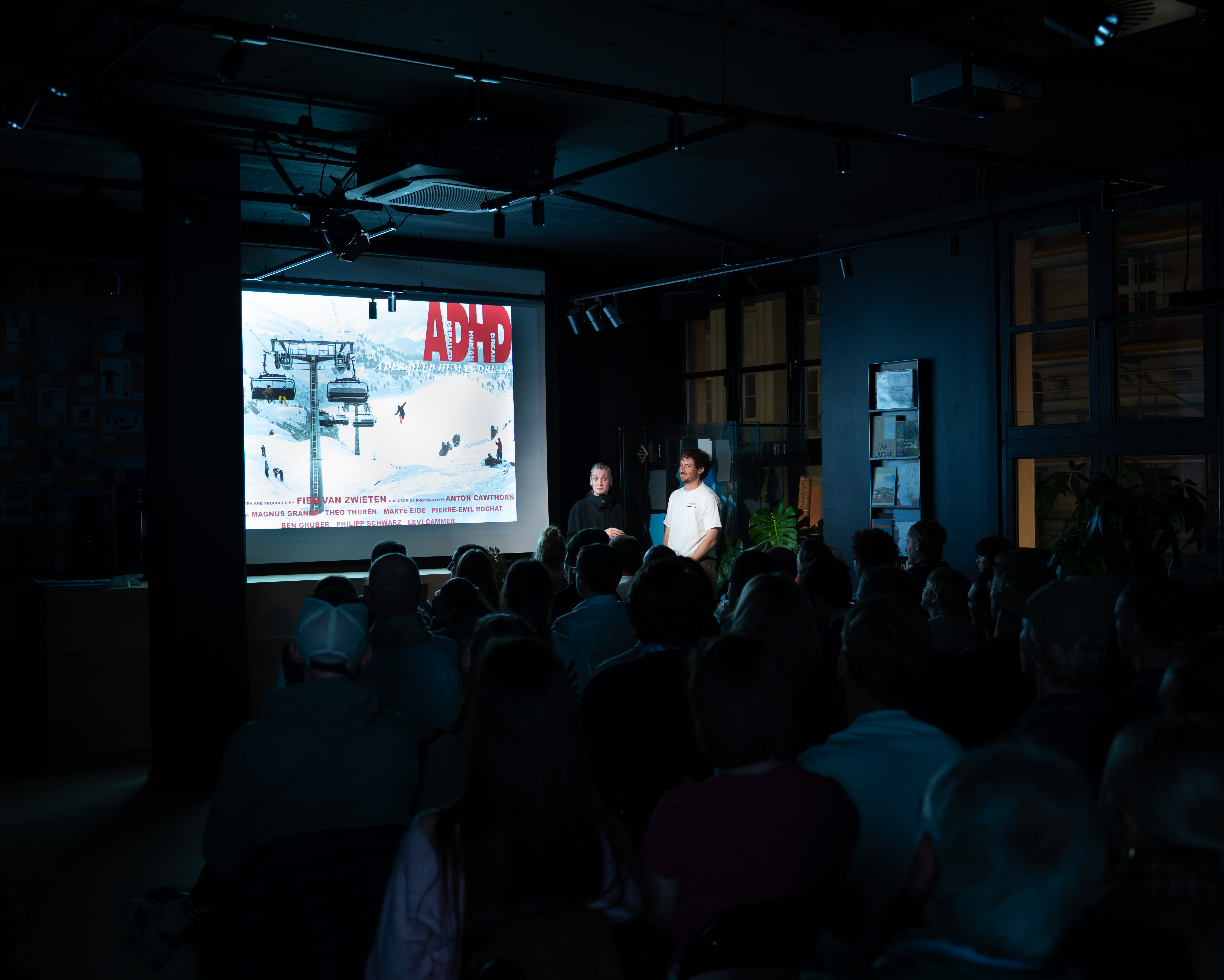 Presenters in Norrøna clothing stand by a screen showing 'ADHD' before a seated audience in a dark venue.