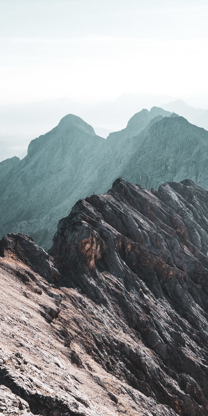 A view from the top of a mountain range. The peaks are covered in fog, creating a dramatic and atmospheric scene. 
