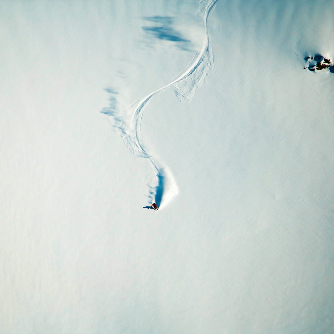 Aerial view of a skier in Norrøna apparel carving a winding path in fresh, white snow.