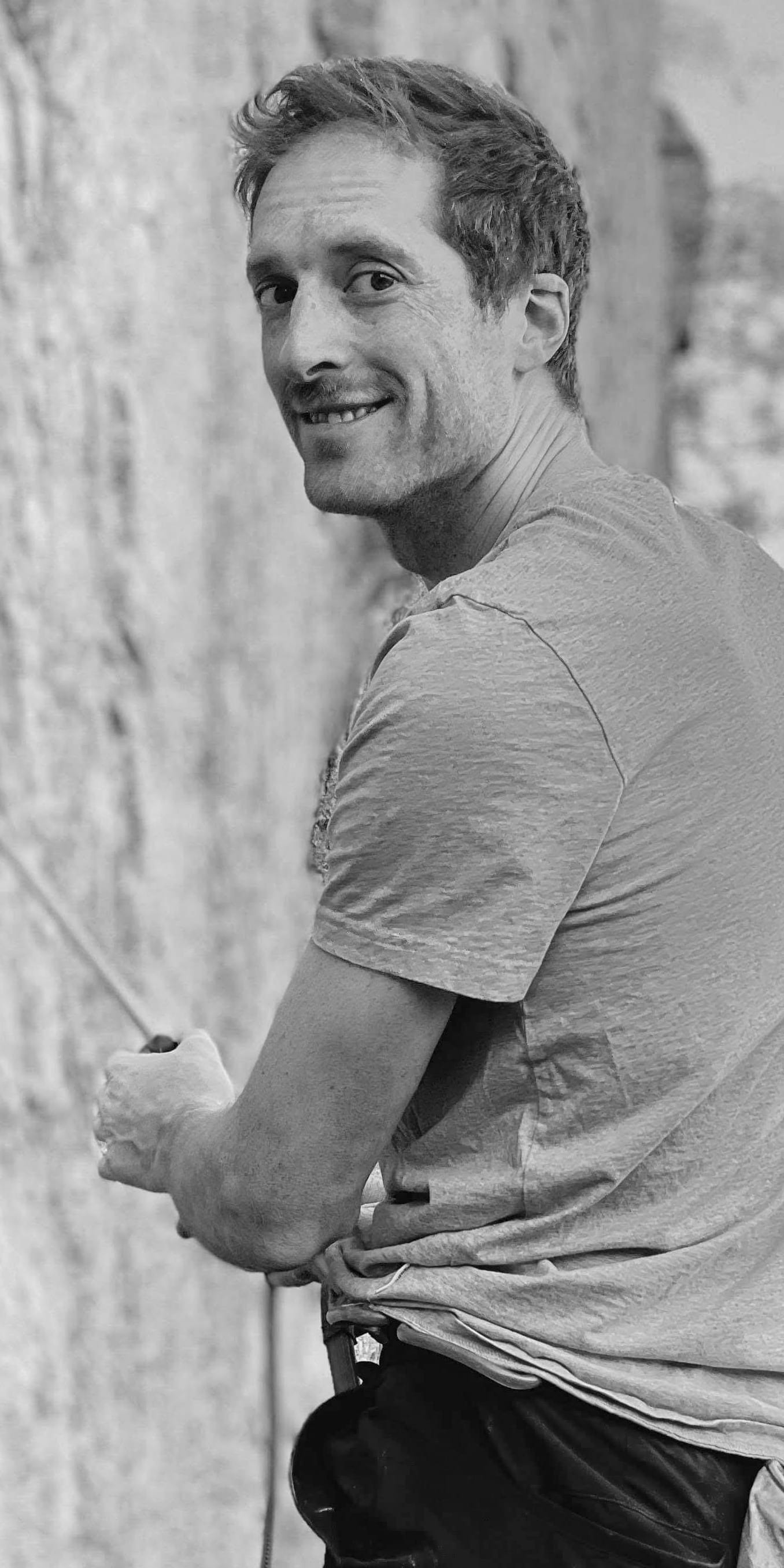 A man in a Norrøna T-shirt and pants smiles while holding a climbing rope.