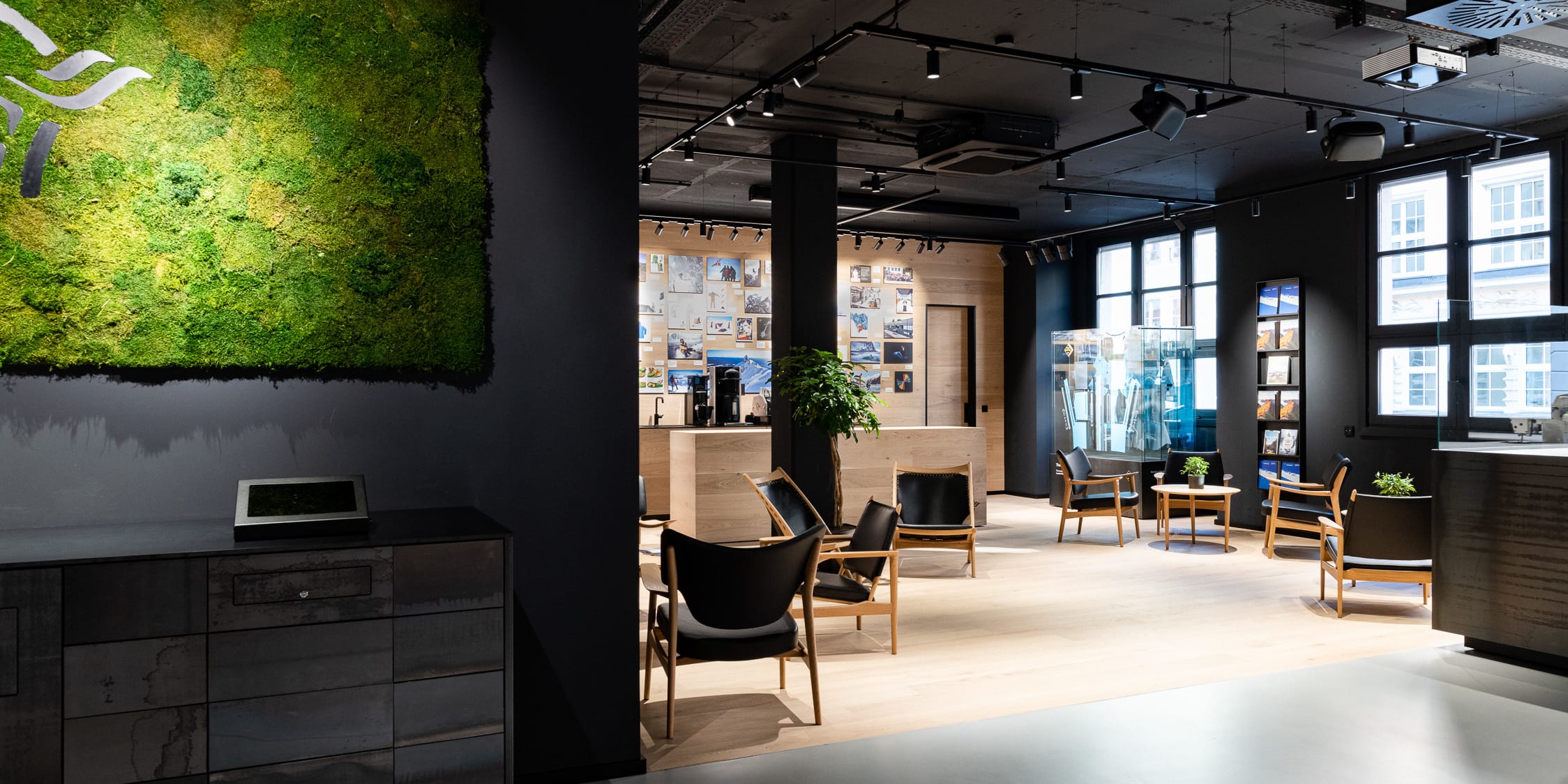 Modern office space with a moss wall, wooden floor, and black Norrøna chairs. 
