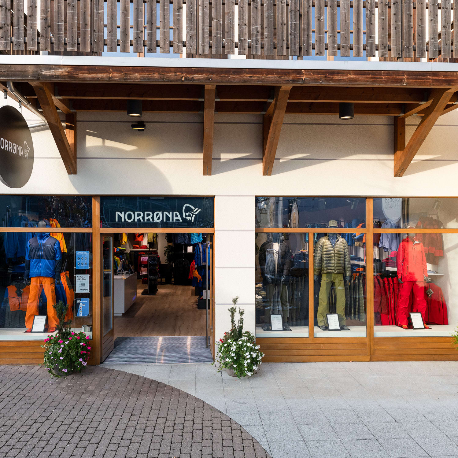 Norrøna storefront with a mannequin wearing a blue jacket and orange pants.  The storefront has large windows displaying Norrøna clothing. 
