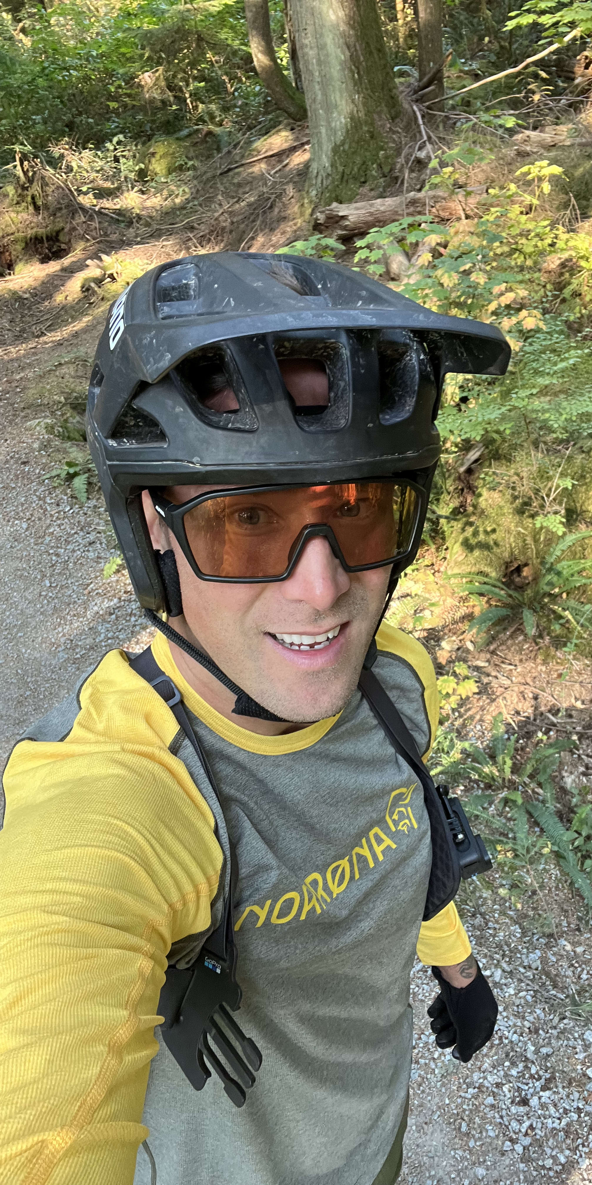 Smiling cyclist wearing a Giro helmet and Norrøna long sleeve jersey on a trail, looking up at the camera.