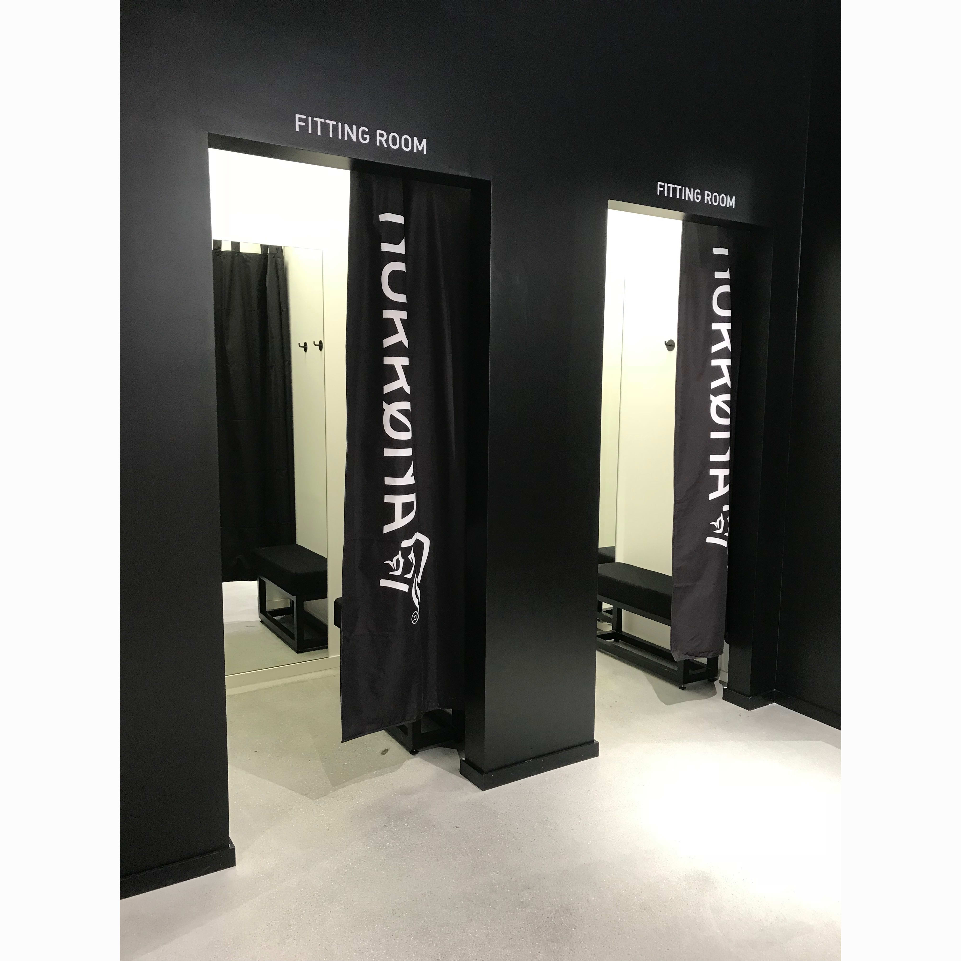 Black fitting rooms with black curtains featuring the white Norrøna logo.