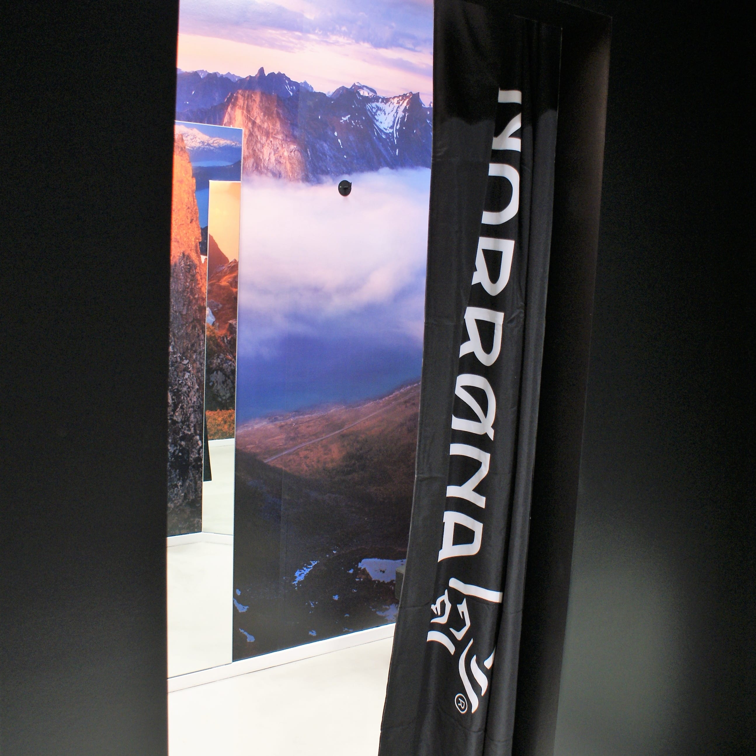 A black Norrøna fitting room curtain in front of a mountain landscape backdrop. 
