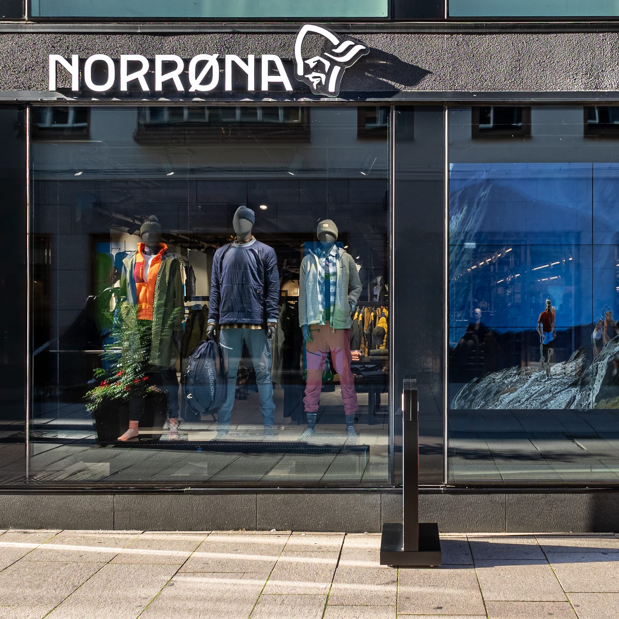 A storefront of a Norrøna store with mannequins displaying outdoor apparel and a picture of a mountain scene with people hiking. 

