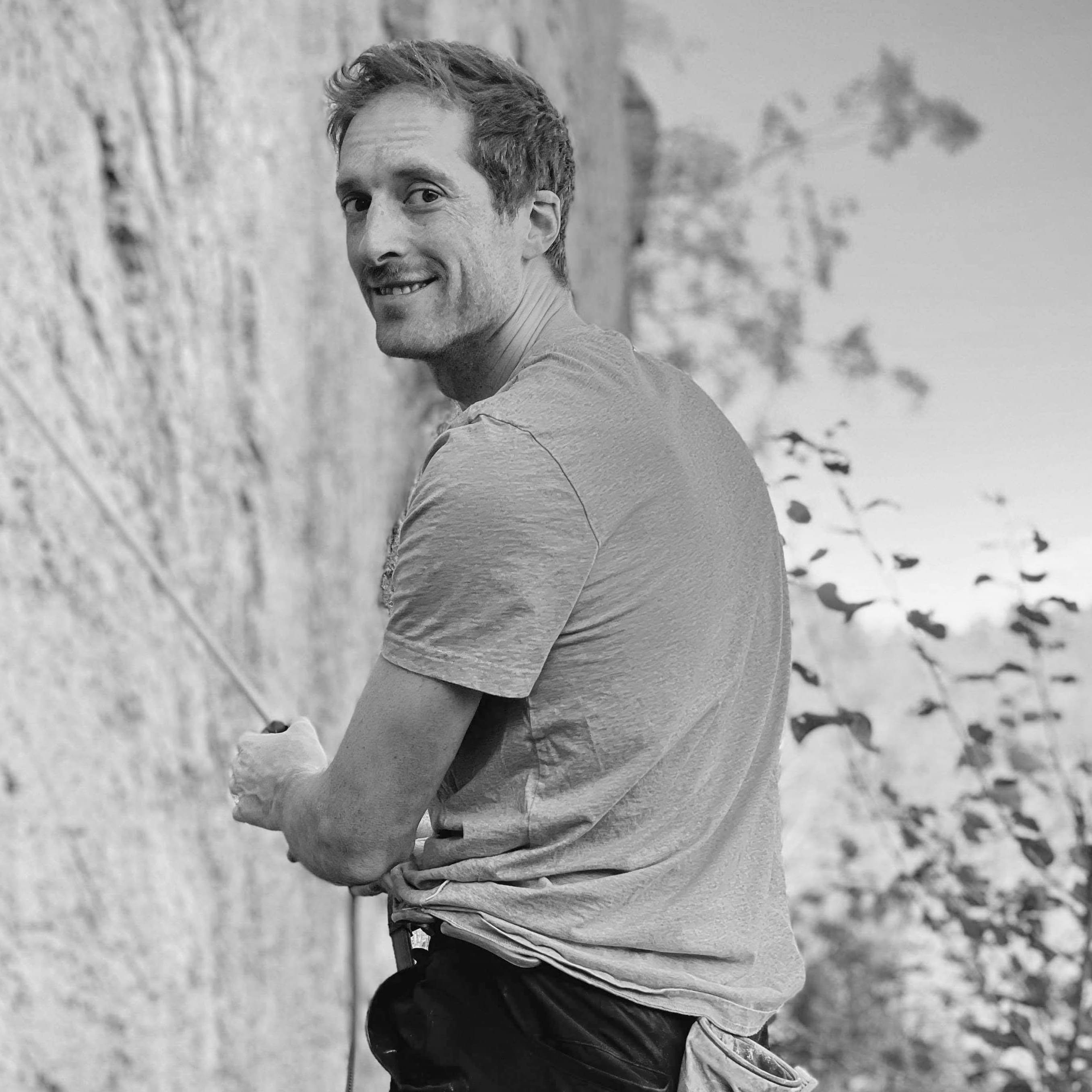 A man in a Norrøna T-shirt and pants smiles while holding a climbing rope.