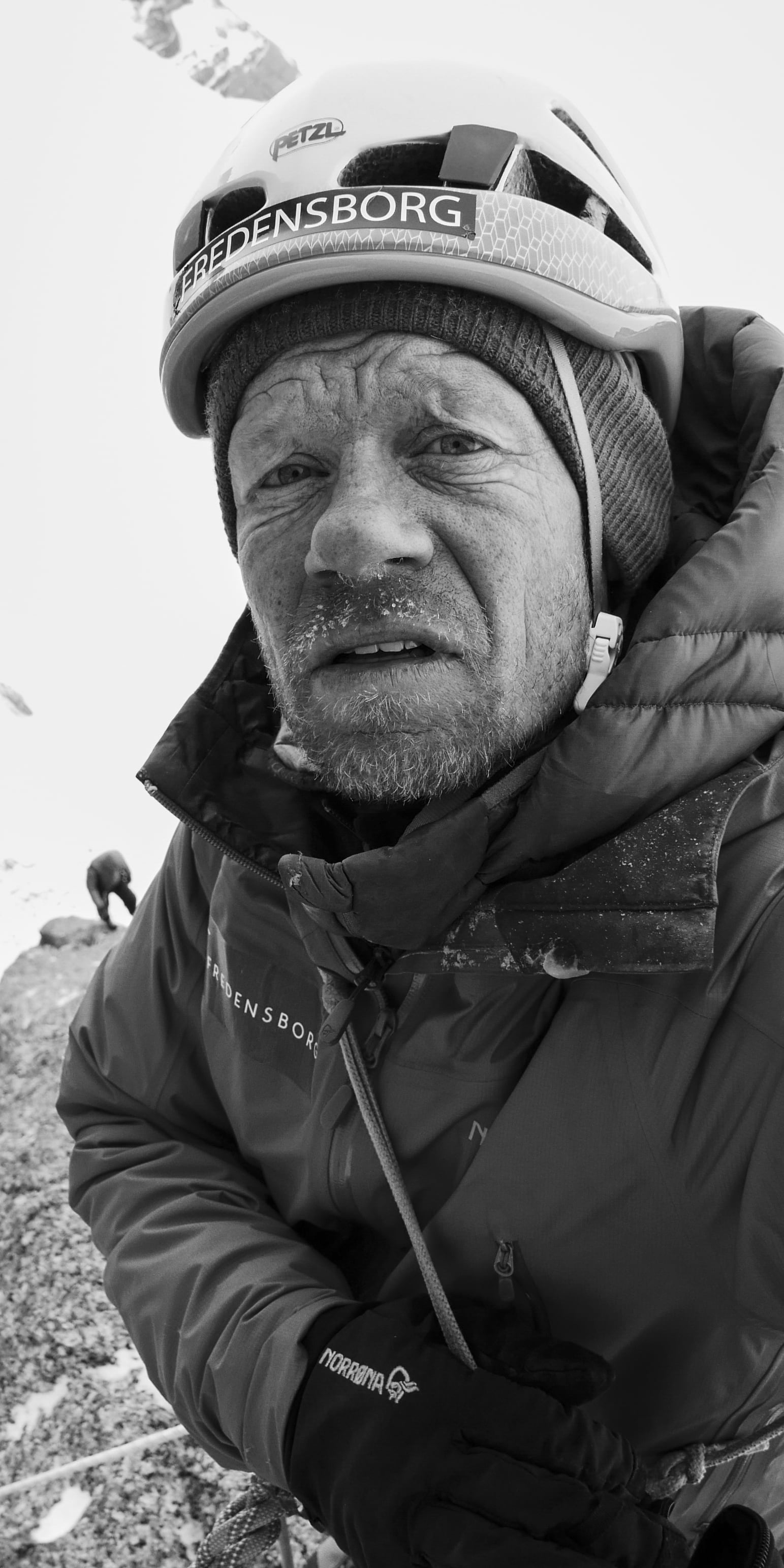 A man in a Norrøna jacket and helmet is climbing a snowy mountain.