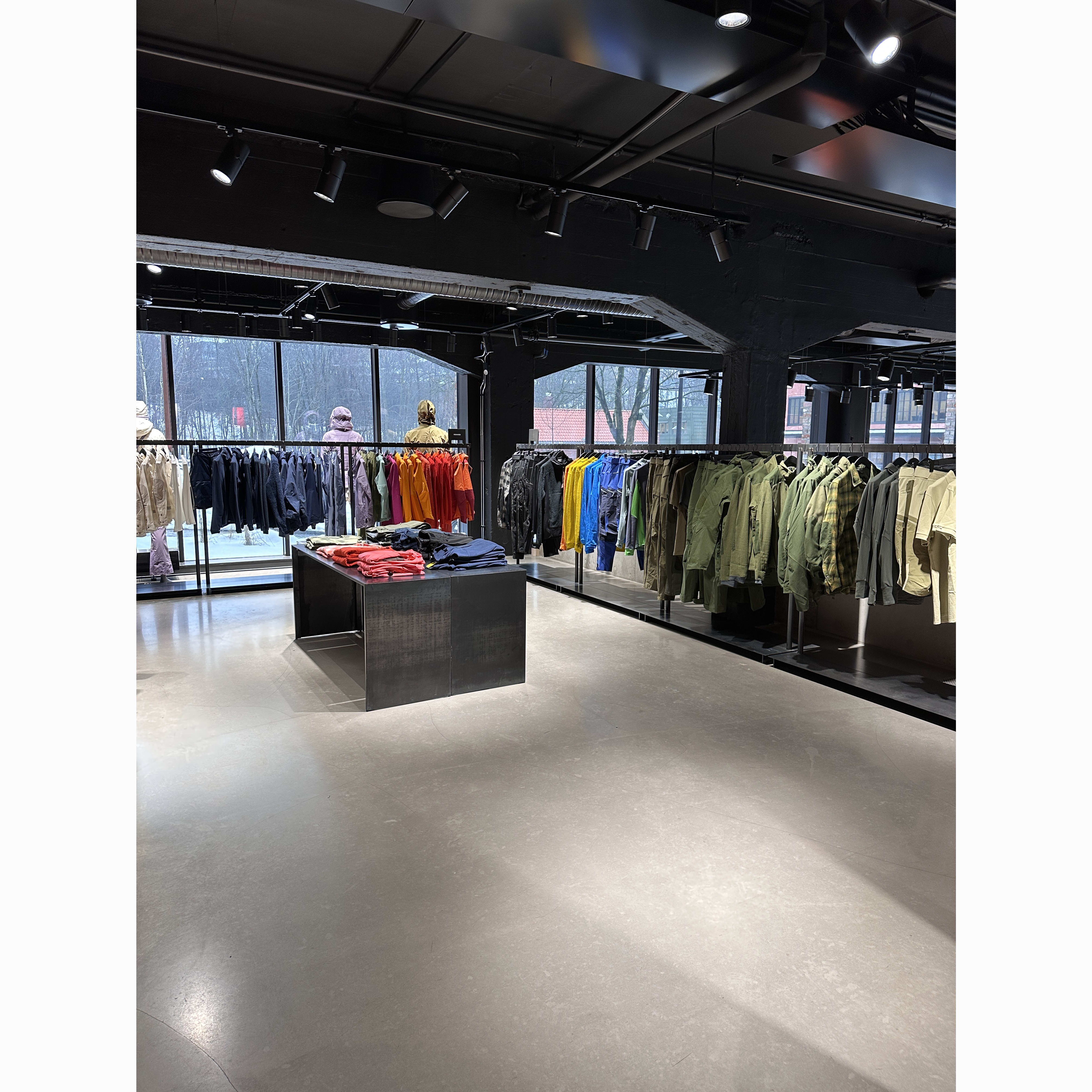 Store interior showcasing Norrøna apparel racks in various colors near a window. Modern design with gray floors and black fixtures.